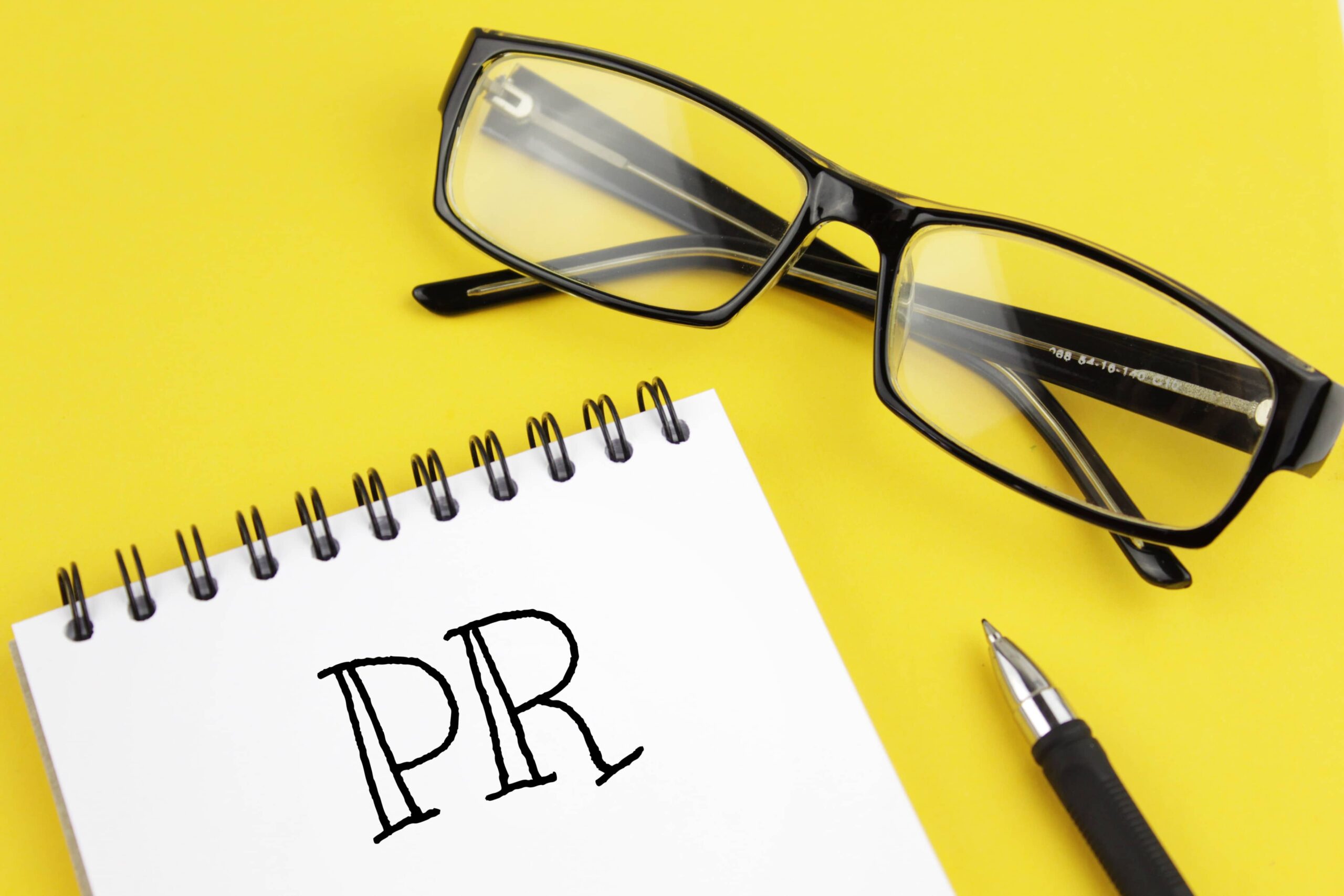 Wykorzystanie influencerów w PR | kartka z napisem PR i okulary na żółtym tle